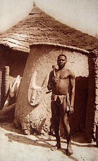 carte postale ancienne représentant un cultivateur samorogouan devant son grenier aux armoiries de son animal fétiche.